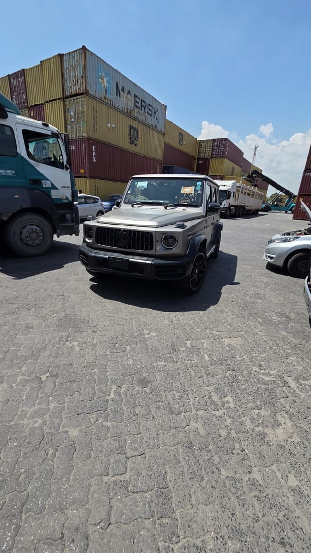 A vehicle waiting for release in a container yard, with stacked containers behind